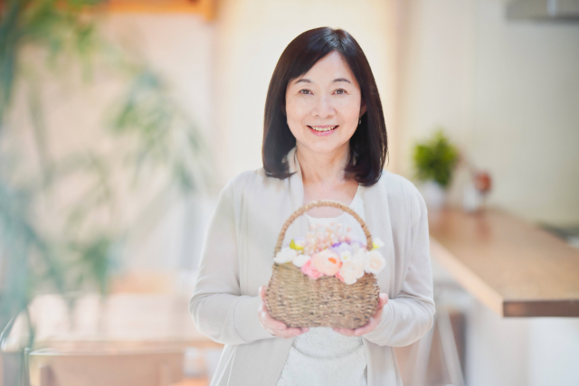 完璧主義を手放しつつある、５０代女性のイメージを花の入ったバスケットを持つ女性の画像で表現