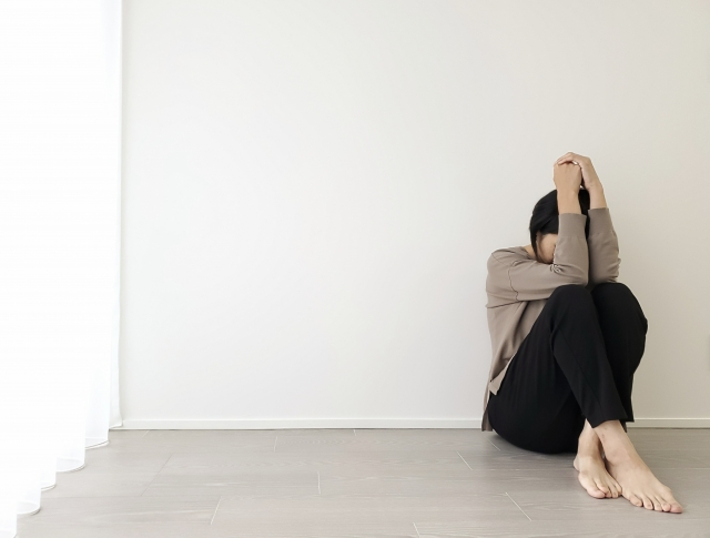 心と身体の緊張が抜けない大人のイメージを部屋の隅で頭を抱える女性の画像で表現