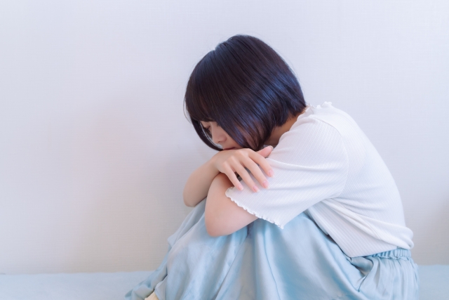 急に泣きたくなる、落ち込むイメージをうつむいて膝を抱えた女性の画像で表現